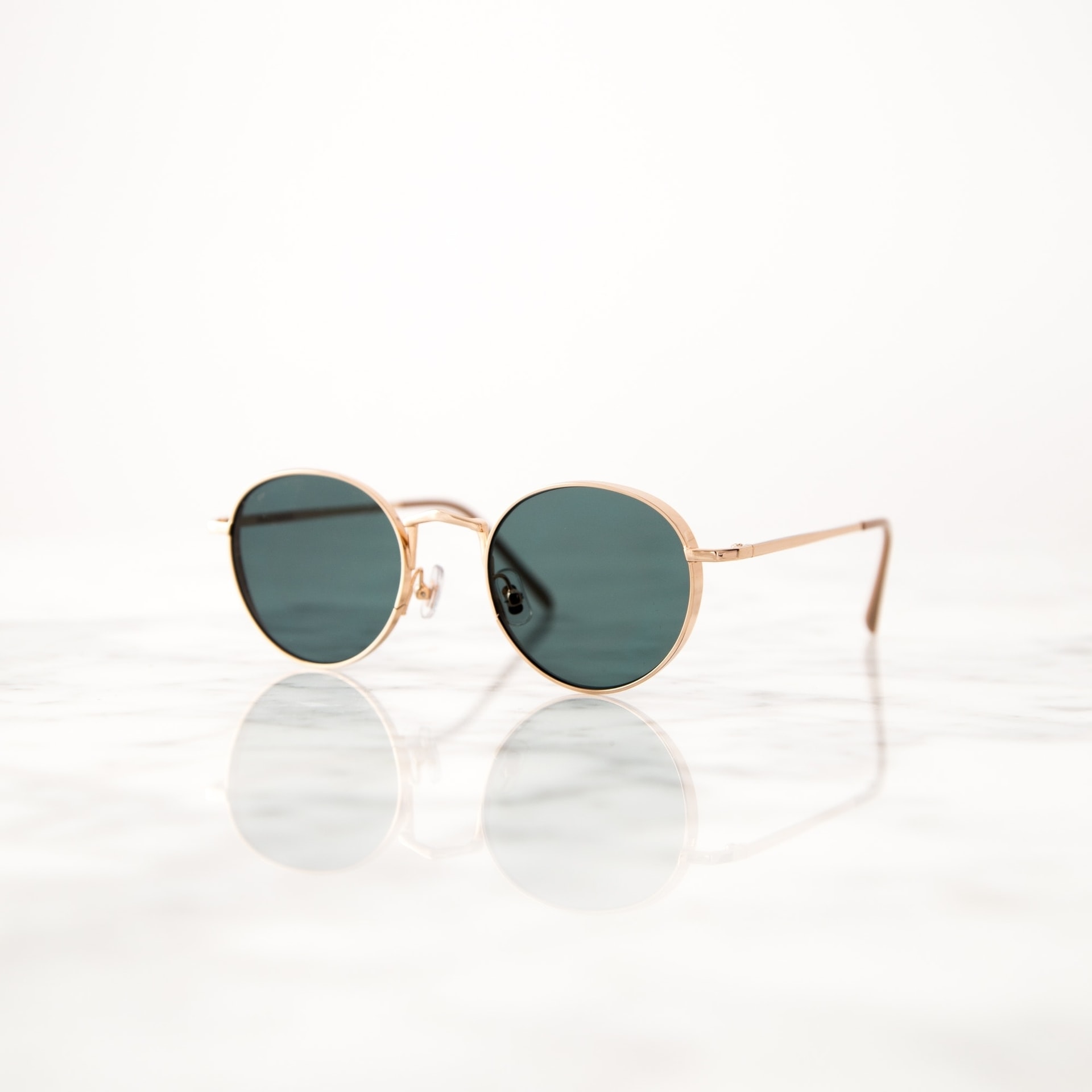 Lunettes de soleil à monture dorée sur surface réfléchissante en marbre